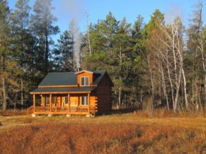 Whispering Pines projects square log home exterior with metal roof and chimney surronded by woods